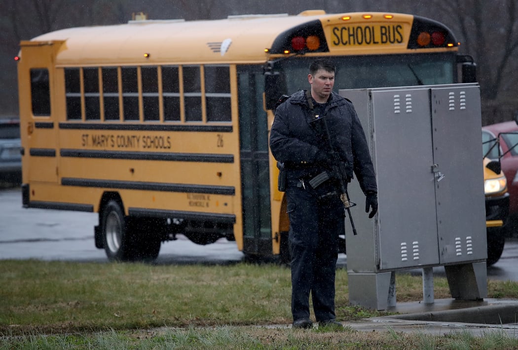 A heavily armed law enforcement officer stands guard as students from Great Mills High School are evacuated.