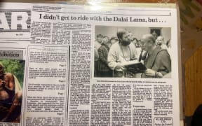 A newspaper clipping with the headline "I DIDN'T GET TO RIDE WITH THE DALAI LAMA, BUT . . ." and a picture showing Dean Schneider handing the Dalai Lama a book.