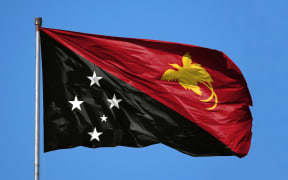 National flag of Papua New Guinea on a flagpole in front of blue sky.