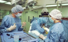 Two surgeons and a nurse perform a thoracoscopy in a hospital operating theatre.