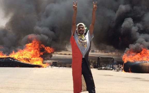 A protester in front of burning tires and debris on the road near Khartoum's army headquarters.
