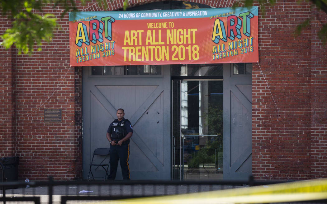 A police officer stands in front as other officers inspect the crime scene at the Roebling Market.