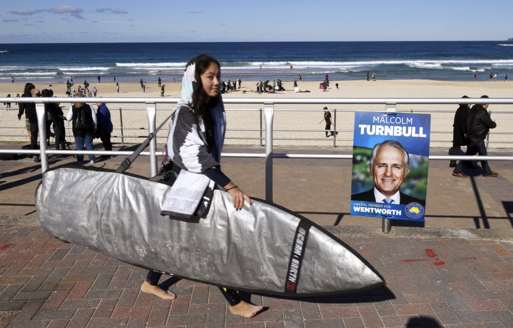 A surfer walks past an election placard outside a voting station in the Sydney suburb of Bondi Beach on July 2, 2016