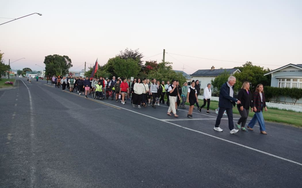 A large group of people walking down a road in Wairoa as the sun rises.