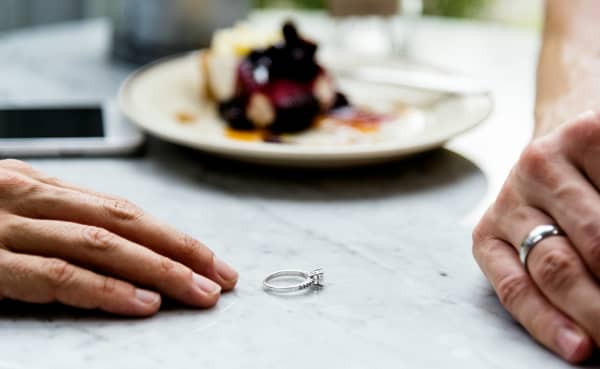 A person leaves their ring on a table where there's another hand wearing a ring.
