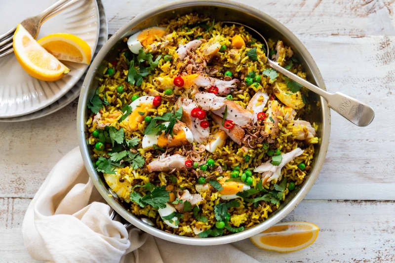 A bowl of kedgeree with lentils, peas, chilli, smoked fish and herbs, garnished with lemon.
