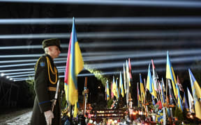 A Ukrainian honour guard stands as a symbolic illumination called "Rays of Memory" is seen over the graves of Ukrainian soldiers, who died in the war with Russia, at Lychakiv Military Cemetery in Lviv on February 23, 2025, on the eve of the third anniversary of Russia's invasion of Ukraine.