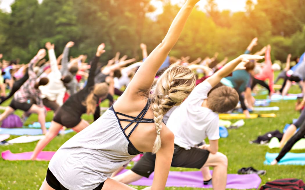 A big group of adults attending a yoga class outside in park