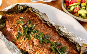 A dish of coconut chilli barbecue salmon on a bed of foil, with asparagus and sweetcorn on dishes in the background.