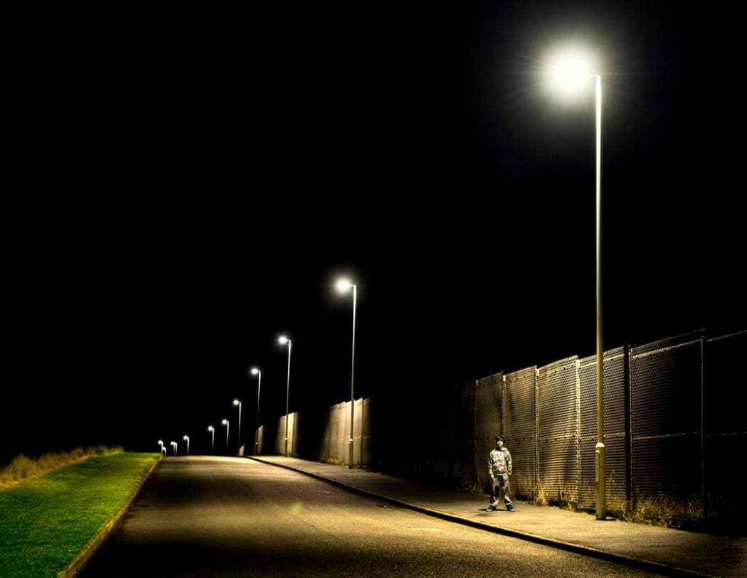 Boy standing on pavement at night with street lights (Photo by Craig Easton / Image Source / Image Source via AFP)