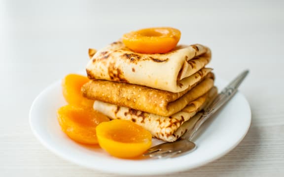 A stack of three folded crepes on a white plate, with some poached apricots.