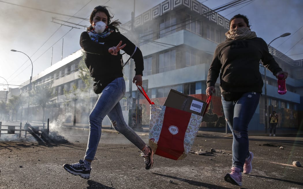 A looter flashes the V sign as she runs during protests in Valparaiso, Chile, on October 20, 2019.
