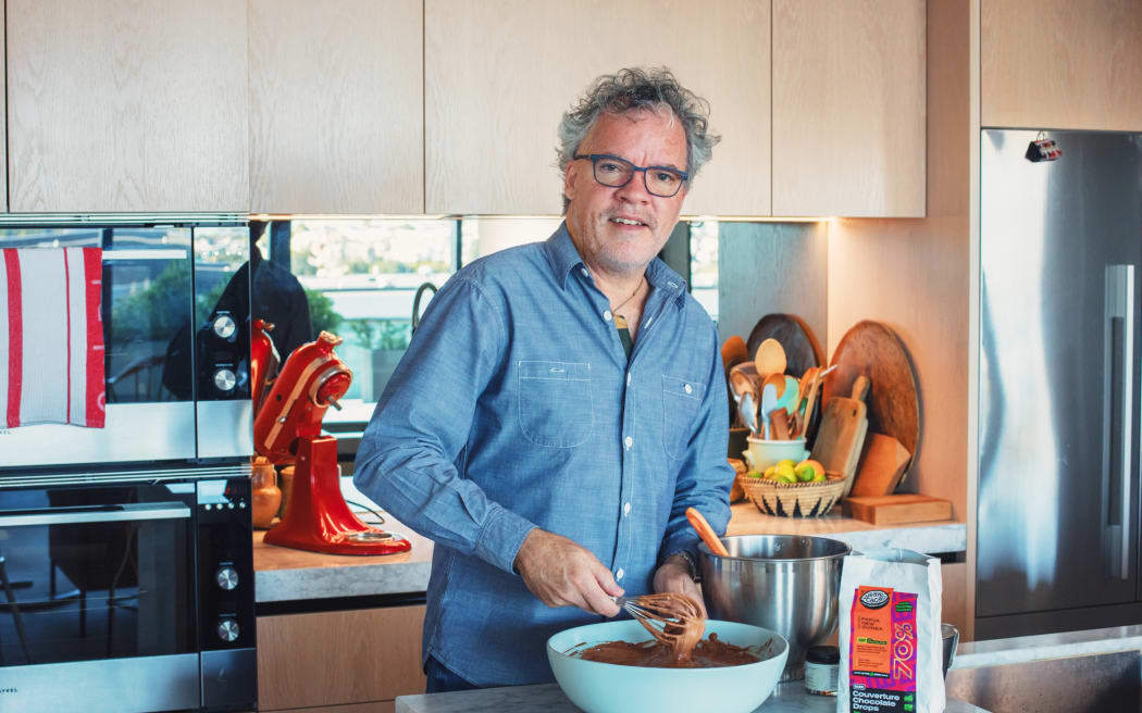 Chef Peter Gordon is whisking a bit bowl of chocolate mousse. Peter is wearing a blue shirt and glasses, and looks towards the camera.