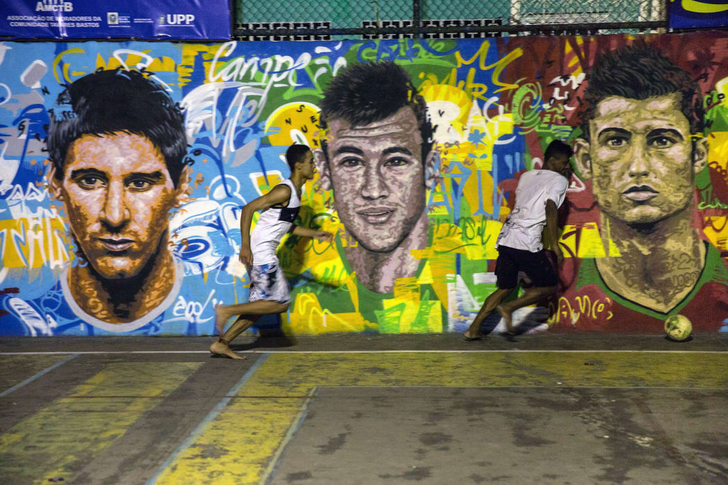Locals play football in front of a mural of soccer stars Lionel Messi (left), Neymar da Silva Santos Junior (centre) and Christiano Ronaldo at a field in a Rio de Janeiro favela.