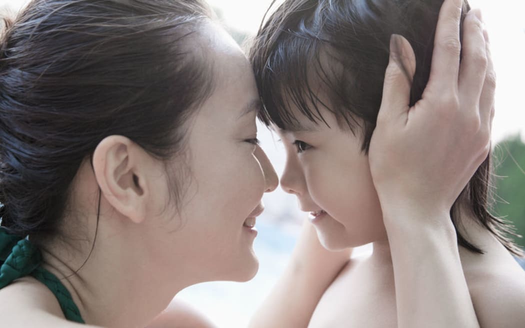 A photo of a smiling mother and son embracing and holding head by the pool