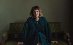 Composer Claire Cowan sits on a green velvet sofa.