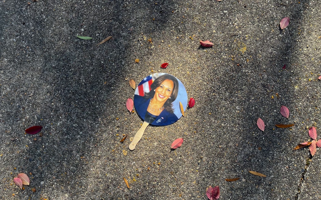 A hand fan depicting US Vice President Kamala Harris lays on a sidewalk in Washington, DC, on November 6, 2024. - Donald Trump won a sweeping victory in the US presidential election, defeating Kamala Harris to complete an astonishing political comeback that sent shock waves around the world. (Photo by Bastien INZAURRALDE / AFP)