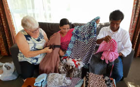 Shenenas Norbasha (centre) showing her creations she's made since receiving the sewing machine from the Red Cross. Pictured with her husband Mohammad (right) and the family's Red Cross volunteer, Esmee Rowden (left).