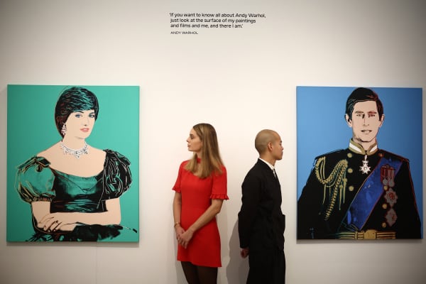 Members of gallery staff study two prints from US artist Andy Warhol, "Portrait of Princess Diana" (L), 1982 and "Portrait of Prince Charles" (R), 1982 during the photocall at the Phillips auction house, in central London, on October 4, 2024 ahead of Modern & Contemporary Art Frieze Week Auctions on 10 and 11 October.