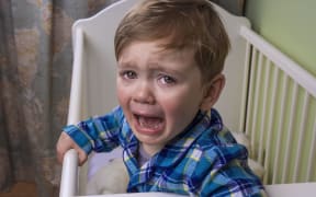 A photo of a small boy having a tantrum at bedtime in his cot
