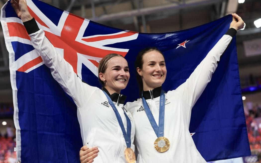 New Zealand's Ally Wollaston celebrates her bronze medal of the women's track cycling omnium event (L) and New Zealand's Ellesse Andrews celebrates her gold medal victory of the women's track cycling sprint event (R) at the end of the the track cycling competition of the Paris 2024 Olympic Games at the Saint-Quentin-en-Yvelines National Velodrome in Montigny-le-Bretonneux, south-west of Paris, on August 11, 2024. (Photo by Emmanuel DUNAND / AFP)