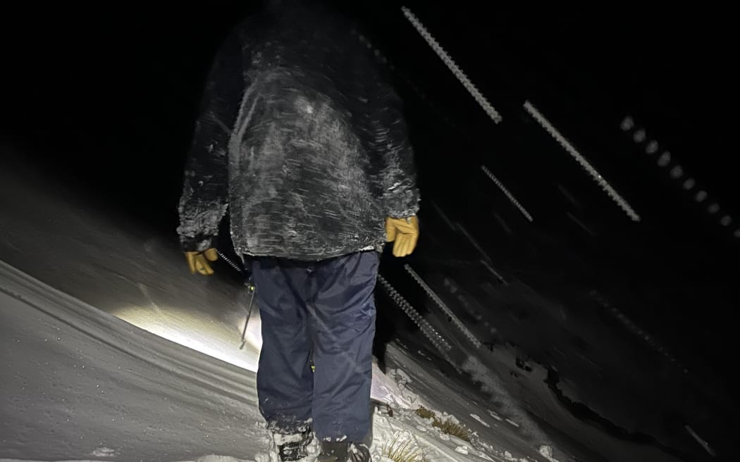 A man walks through snow and darkness on the Tongariro Alpine Crossing.