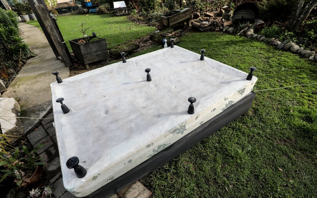 A damaged bed is upturned outside a flooded home