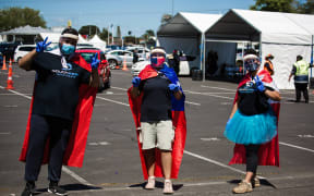 South Seas helpers drape flags across them as they support the Ōtara community at the Super Saturday vaccination event