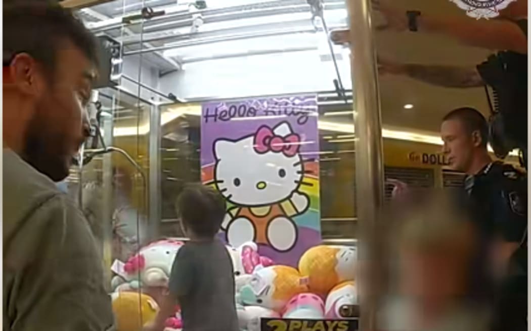 Three-year-old Ethan Hopper stuck inside a claw machine while his dad and police look on.