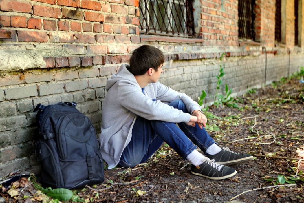 A photo of a sad teenage boy sitting on the grass near an old brick building