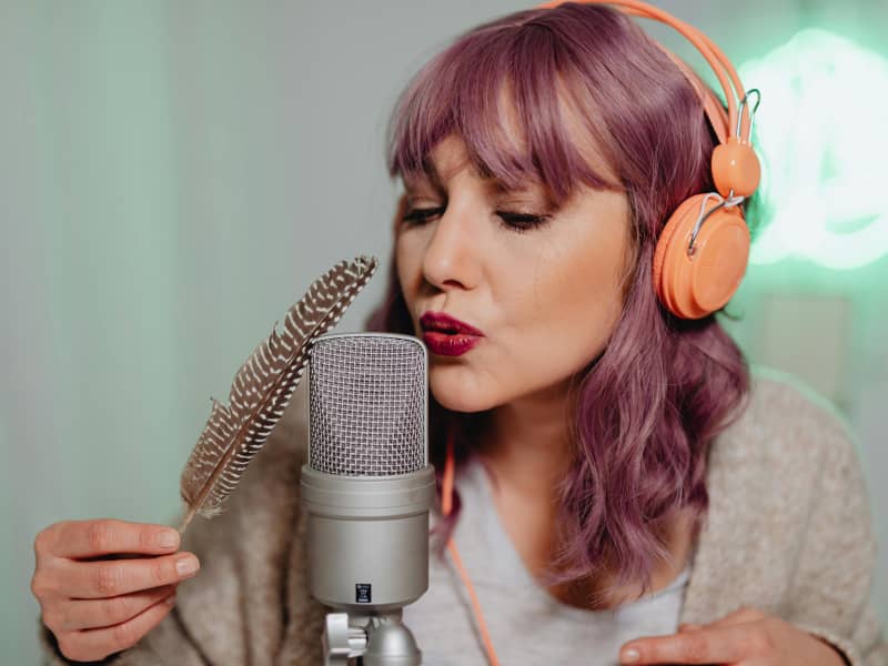 A woman with pink hair blows into a microphone.