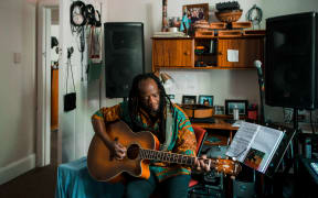 Judah Seomeng playing guitar in his house in Te Whanganui-a-Tara
