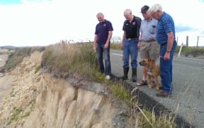 Residents survey the erosion that has partially closed the coastal route.