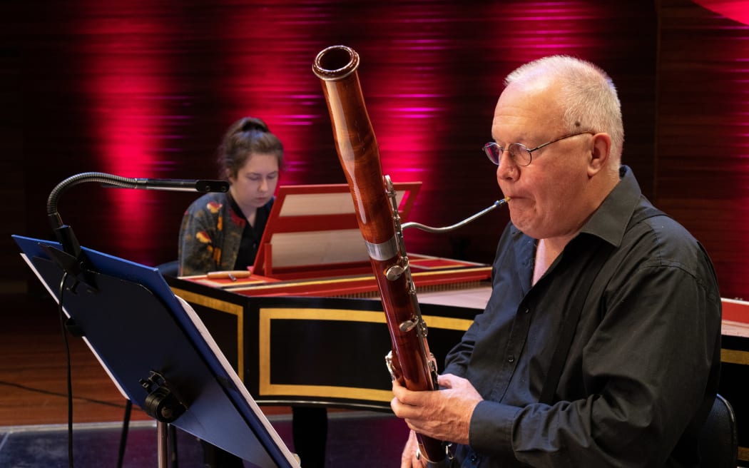 NZSO bassoonist David Angus playing his instrument. A pianist accompanies him in the background.