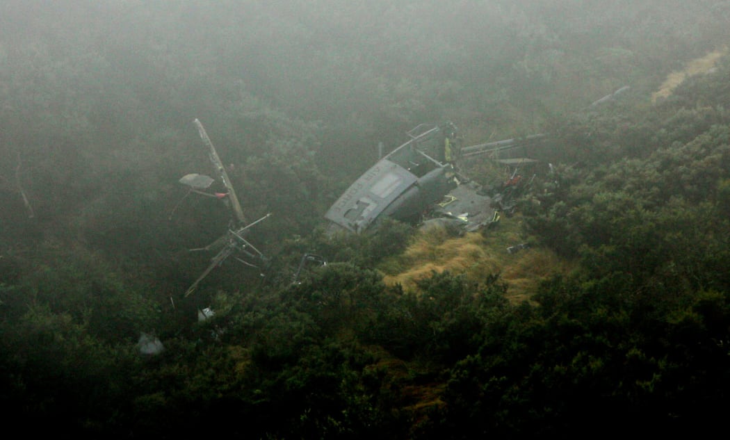 The wreckage of NZ3806 on the side of the ravine. The helicopter is lying on its right hand side, has broken in two and slightly covered by mist.