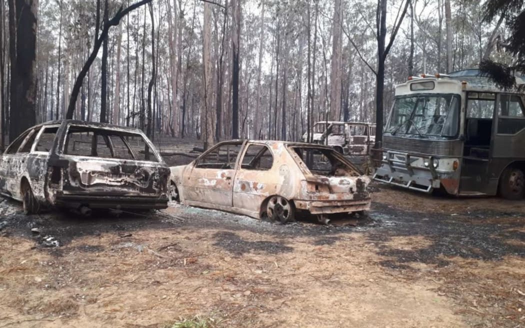 Priscilla Queen of the Desert bus next to burnt out cars in the bush.