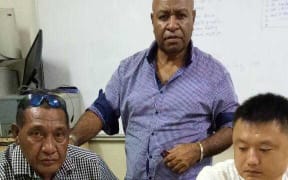 PNG Police Investigations Team Leader Senior Sergeant Apollos Terry (standing) with suspect Zhiyaun (Aaron) Cui (seated right) with the K10,000 cash allegedly offered to Senior Sergeant Terry (left)