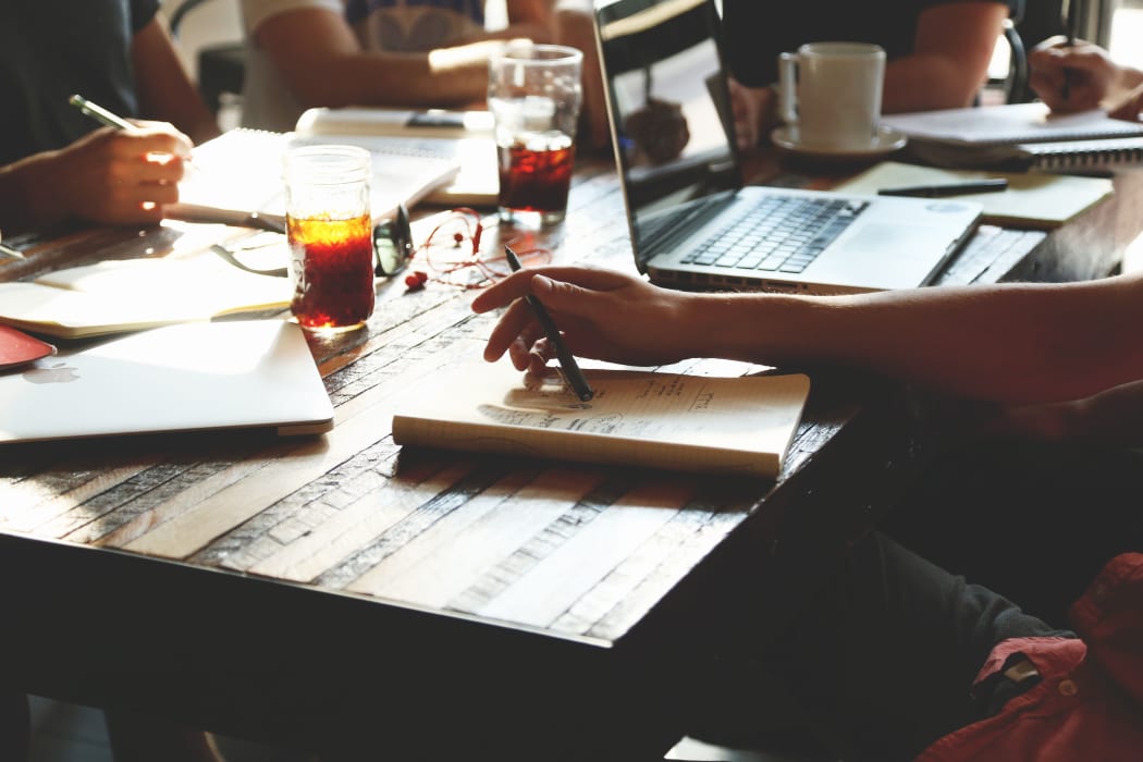 people studying meeting at a table with books, coffee, drink, pen, laptop.