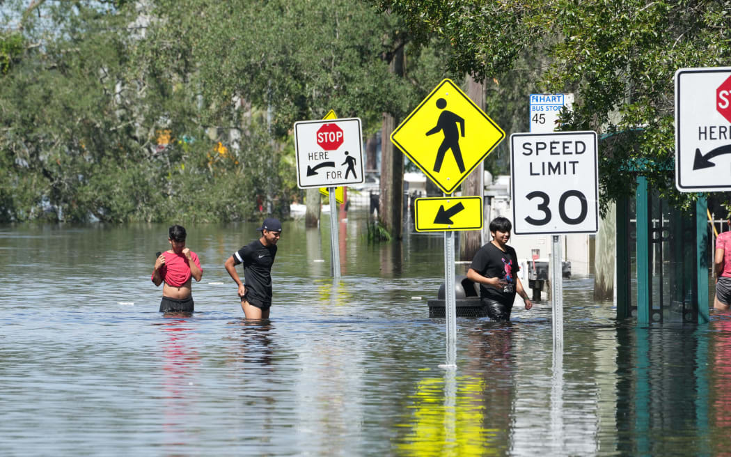 Children walk in the water as the  streets are flooded in the Southeast Seminole Heights section of Tampa, Florida, due to Hurricane Milton on October 10, 2024. - Hurricane Milton tore a coast-to-coast path of destruction across the US state of Florida, whipping up a spate of deadly tornadoes that left at least four people dead, but avoiding the catastrophic devastation officials had feared. (Photo by Bryan R. SMITH / AFP)