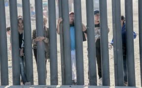 Honduran caravan members look through through the fence at the US-Mexico border wall in San Ysidro on November 18, 2018.