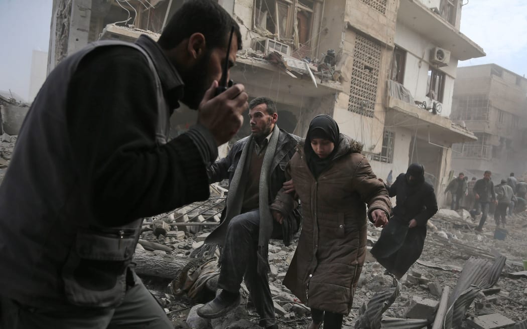 A member of the Syrian civil defence speaks on a wireless transmitter as other civilians flee from an area hit by a reported regime air strike in the rebel-held town of Saqba, in the besieged Eastern Ghouta region on the outskirts of the capital Damascus, on February 20, 2018.