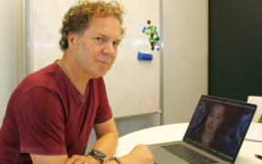 Greg Cross of Soul Machines sits in front of a laptop with the image of the digital human  "Rachel" on screen