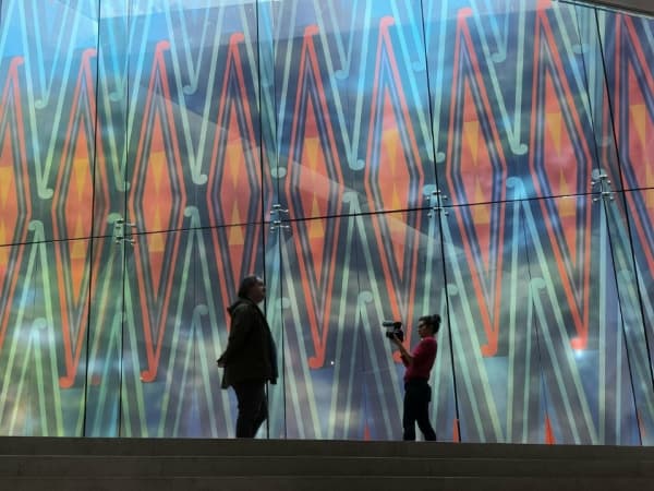 Two silhouetted figures stand in front of a large colourful artwork.
