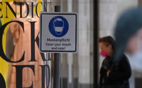 A pedestrian wearing face mask walks past a mask required sign Munich, southern Germany, on 23 March 2021.
