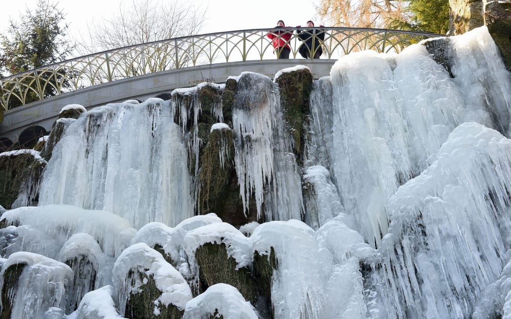 People standing on a bridge above a frozen waterfall at the Bergpark Wilhelmshoehe park in Kassel in central Germany.
