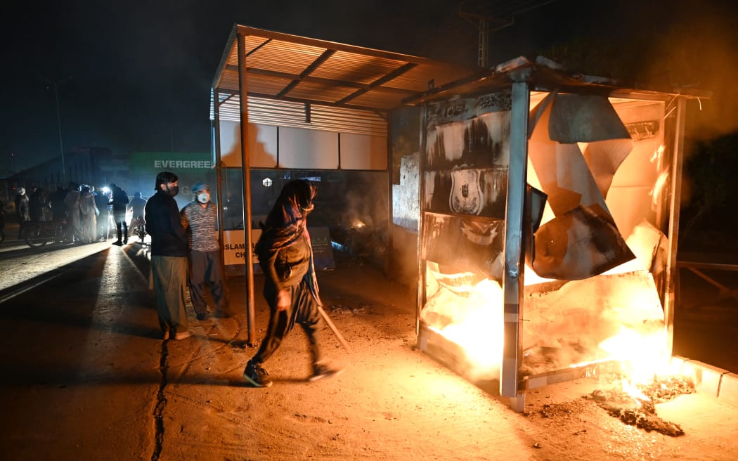Suporters of jailed former prime minister Imran Khan's Pakistan Tehreek-e-Insaf (PTI) party stand beside a burning police checkpoint amid clashes with security forces, during a protest demanding his release in Islamabad late on November 25, 2024. - Pakistan's capital was under total lockdown on November 24, with mobile internet cut and thousands of police flooding the streets as supporters of jailed ex-prime minister marched on the city. (Photo by Aamir QURESHI / AFP)