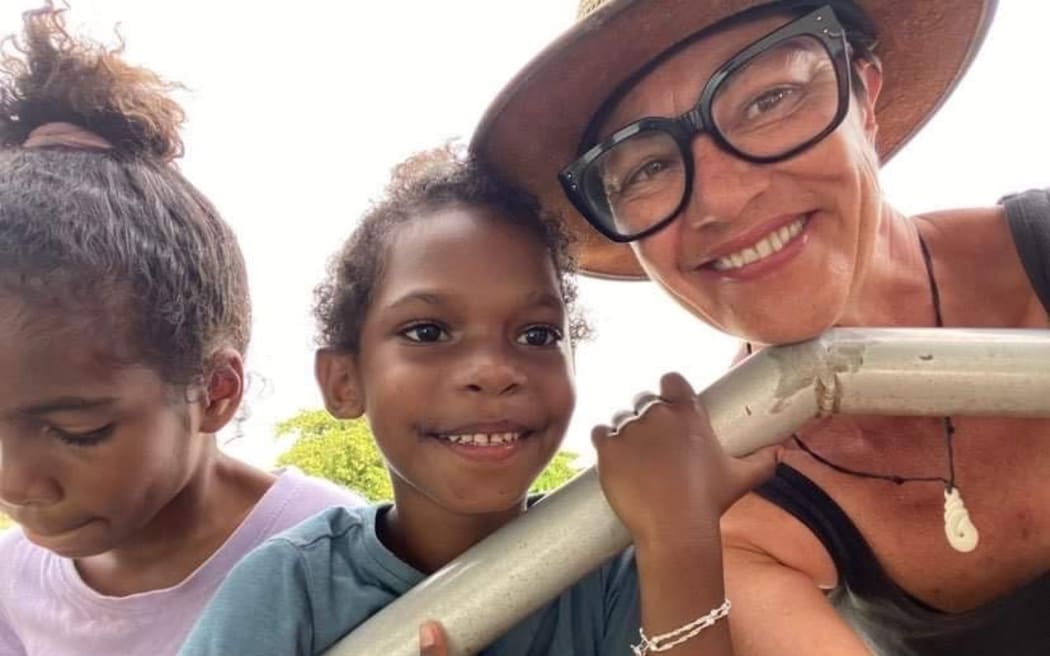 Kiwi nurse Sandra McMullan (right) with two local children in Bamaga, in north Queensland. Sabdra is wearing a hat and she has black-framed glasses. One of the children is looking at the camera, the other is looking down.