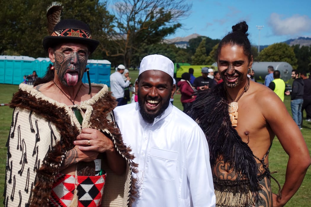 A member of the Muslim community poses with Maori men clad in traditional dresses as people gather for prayers and to observe a two minutes of silence for victims of the twin mosques massacres at Hagley Park in Christchurch on March 22, 2019. (Photo by Jerome TAYLOR / AFP)