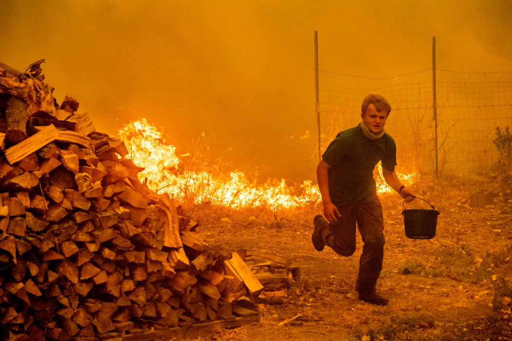 Alex Schenck, 15, carries a water bucket while fighting to save his home as the Ranch Fire tears down New Long Valley Rd in California.
