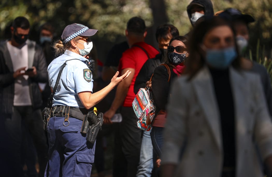 A New South Wales police officer wearing a face mask talks with people as they stand in a line waiting to be vaccinated at the Sydney Olympic Park Vaccination Centre at Homebush in Sydney on August 16, 2021. (Photo by DAVID GRAY / AFP)